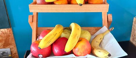 Un puesto de madera con manzanas, plátanos y naranjas.