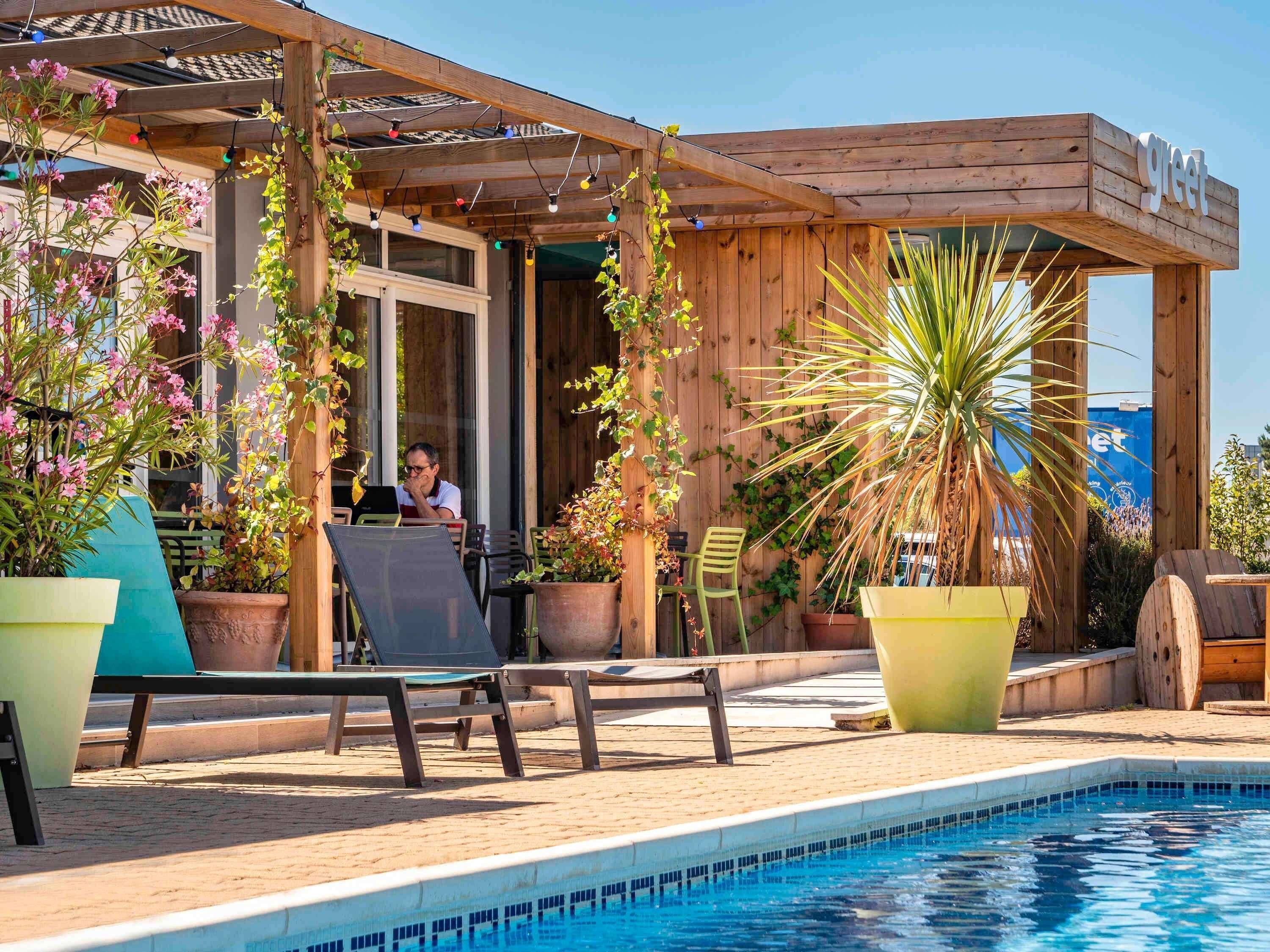 A poolside area with a wooden pergola, outdoor seating, and a sign that reads 'greet'.