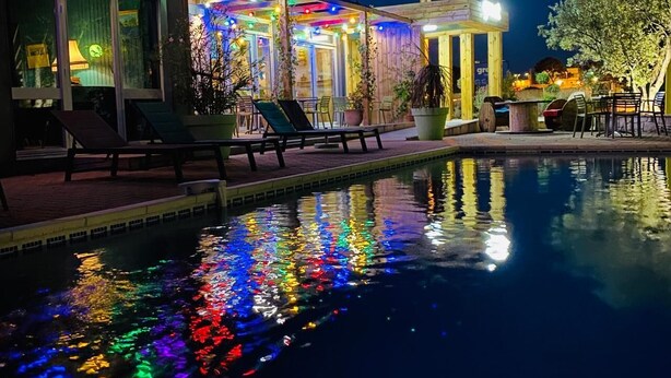 Un espace aménagé au bord de la piscine, avec des chaises longues et un bâtiment illuminé de lumières colorées.