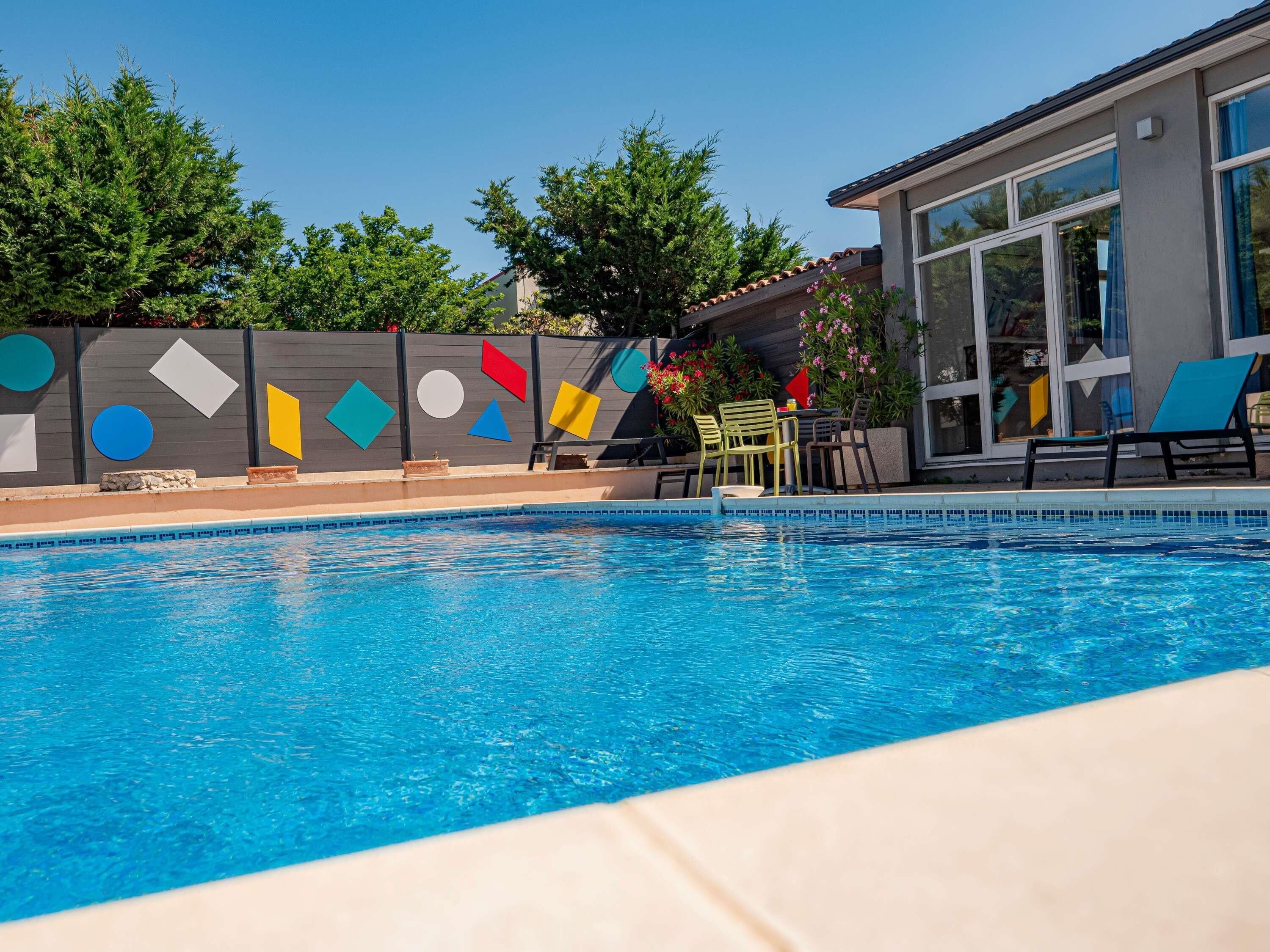 Una piscina con borde de azulejos, rodeada por una valla de diseños geométricos.