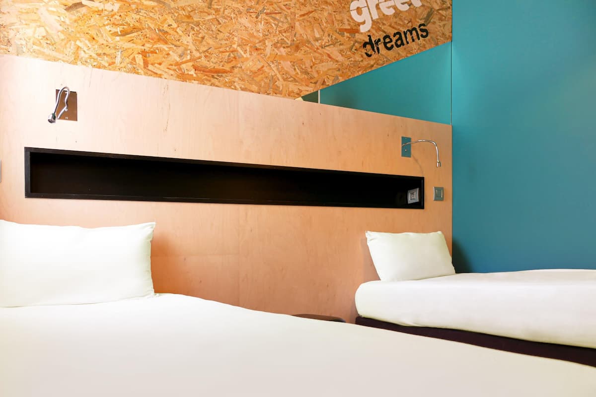 Habitación de hotel con dos camas, cabecero de madera, repisa negra y pared de acento color aguamarina.