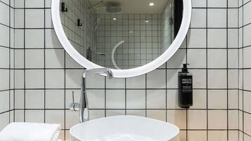Un baño con espejo redondo, lavamanos y toalla.