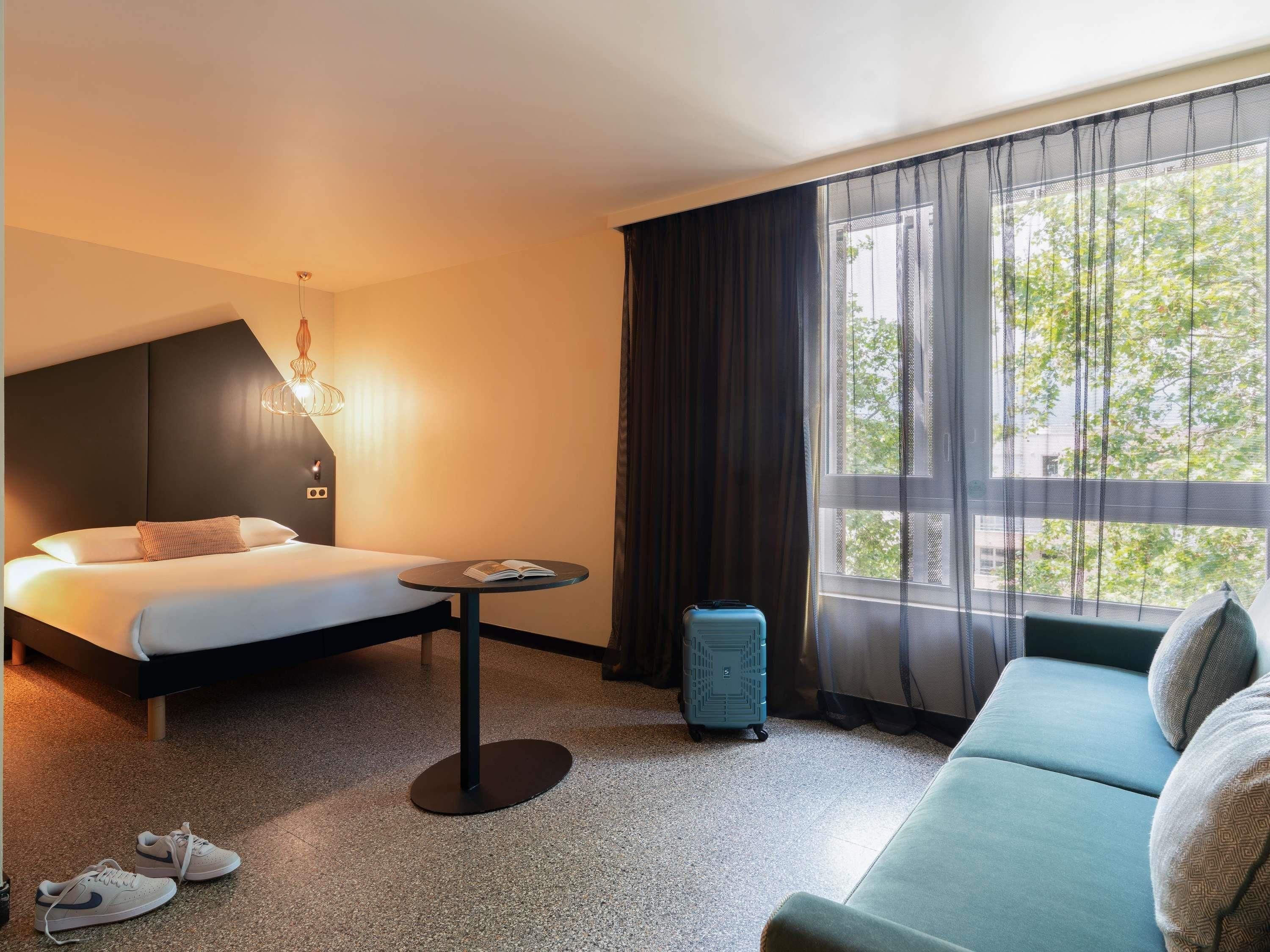 Una habitación de hotel con cama, una mesita, un sofá y una maleta.