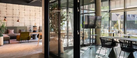 A modern interior with a glass door leading to an outdoor seating area, a sofa, and a dining table with chairs.