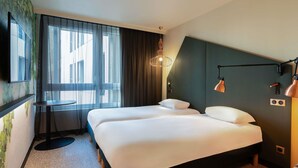 A hotel room with a bed, a desk, and a large window with curtains.