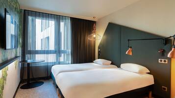 A hotel room with a bed, a desk, and a large window with curtains.