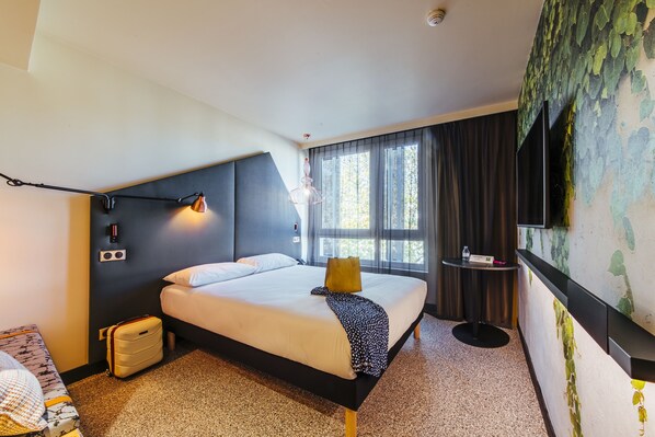 Ett modernt hotellrum med en stor säng, ett sängbord, en lampa, en resväska och ett fönster med gardiner.