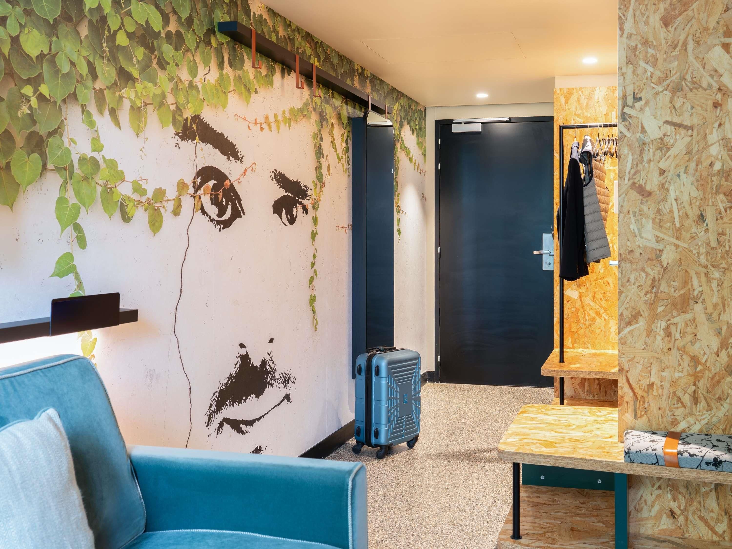 A room with a blue sofa, a small table, a suitcase, and a coat rack with a jacket.