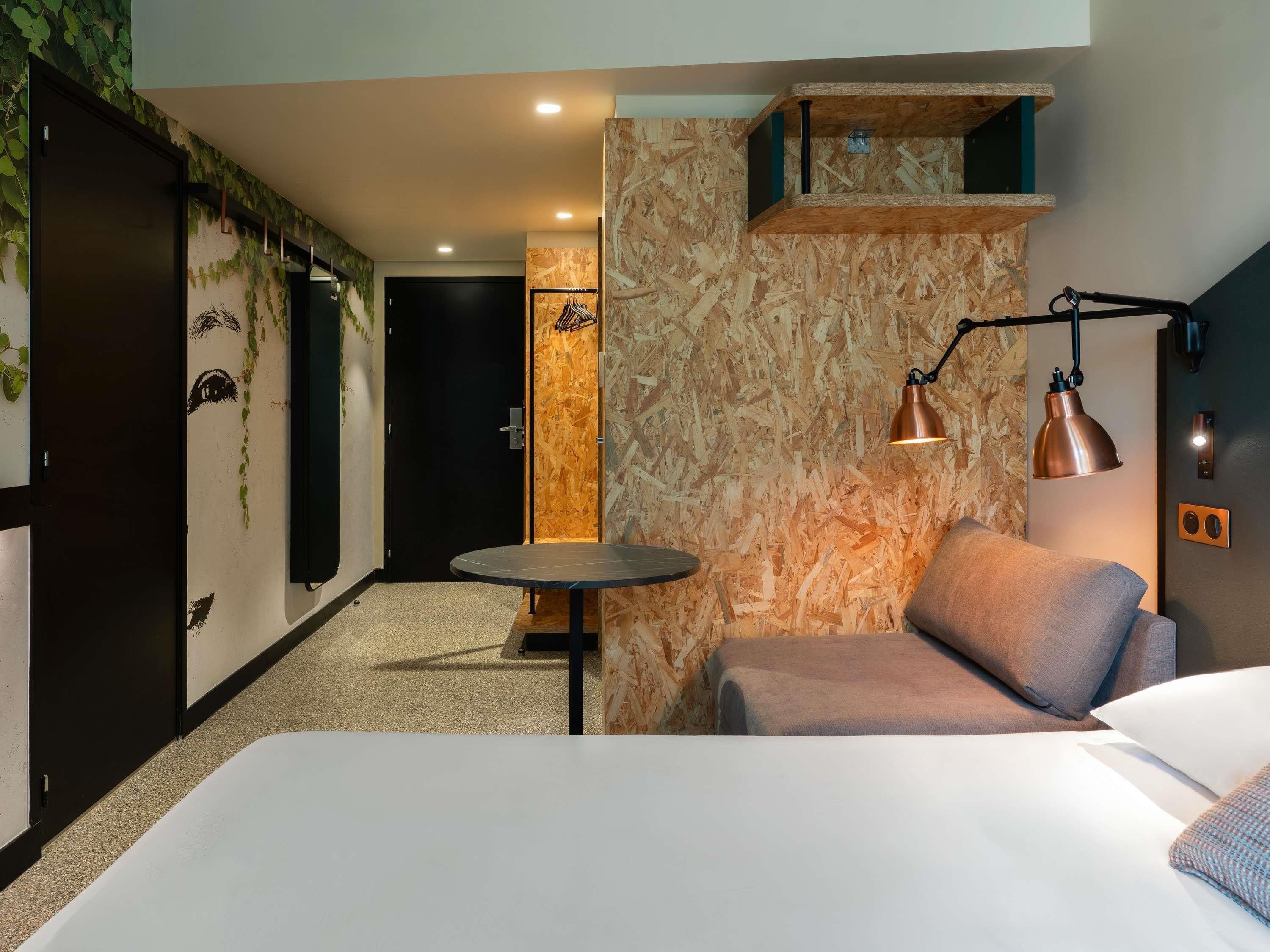 A hotel room with a bed, a small round table, a sofa, and a wall-mounted shelf.