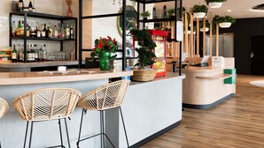 A bar area with a counter, bar stools, shelves with bottles, and decorative plants. - ibis Styles Rouen Centre Rive Gauche  (Rouen)