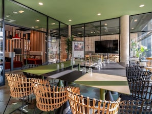 Un comedor interior moderno con mesas y sillas, una pantalla grande y un techo verde.