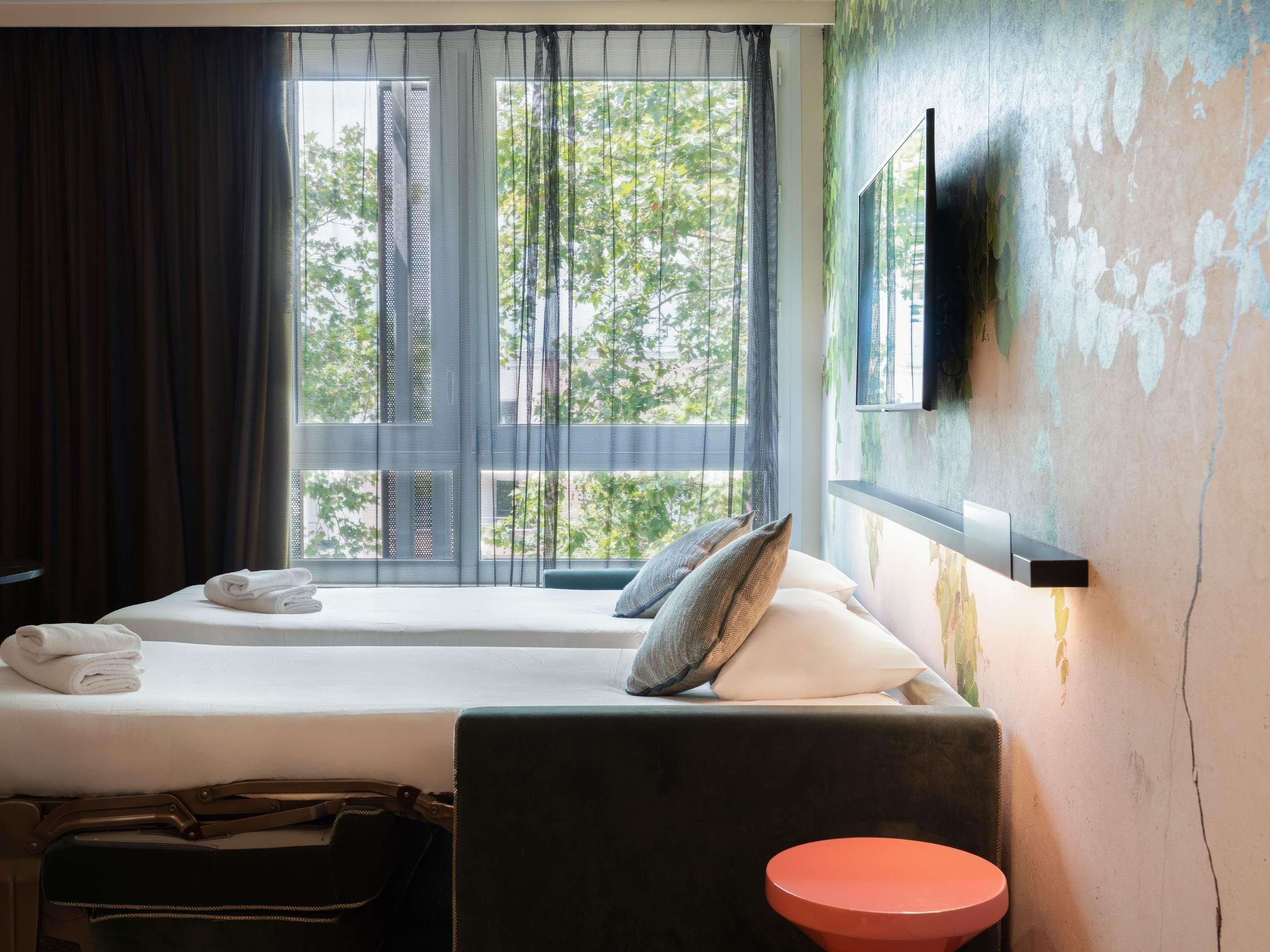 Une chambre d’hôtel avec deux lits, un téléviseur fixé au mur et une fenêtre avec des rideaux.