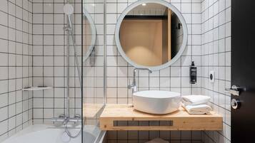 Un baño moderno con ducha de vidrio, un espejo redondo, un lavamanos blanco y un mueble de tocador de madera.