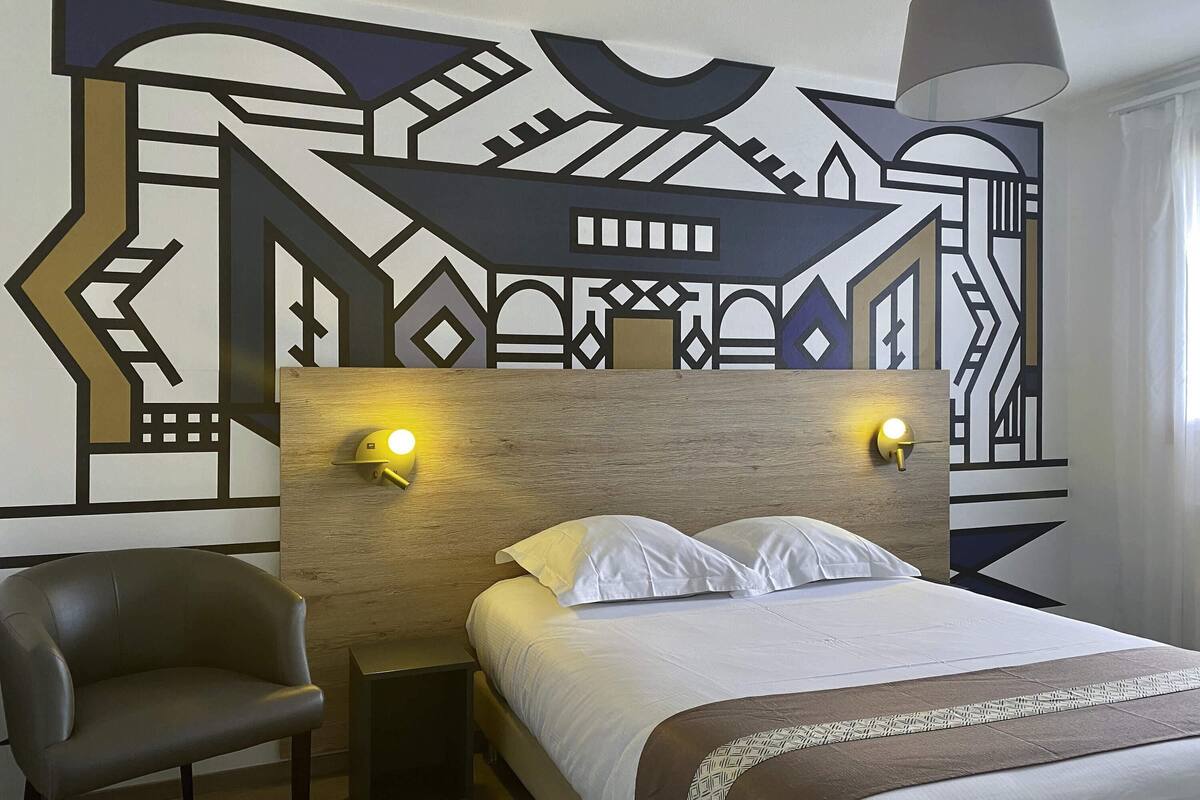 A hotel room with a bed, two bedside lamps, a chair, and a decorative wall.