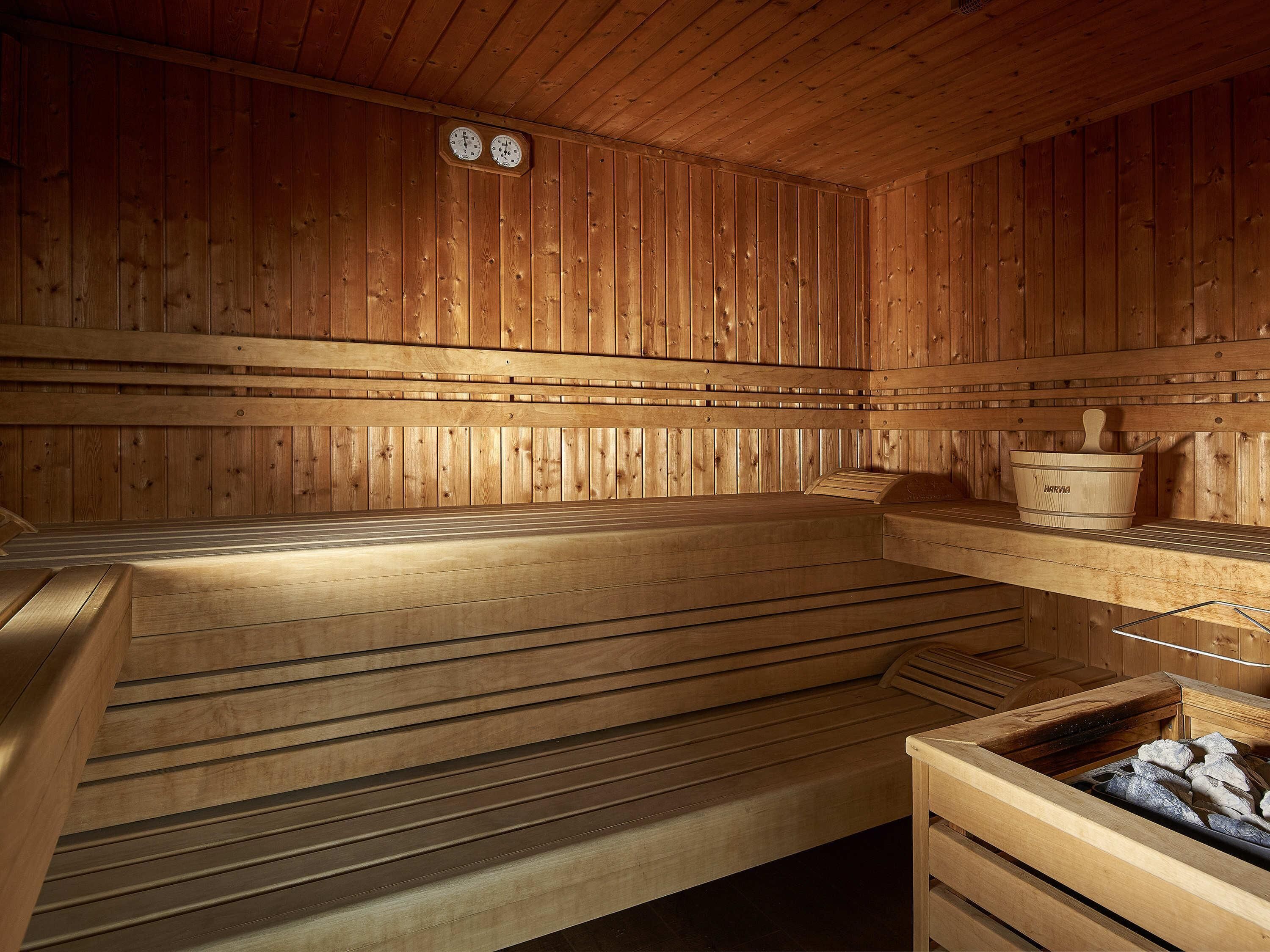 A wooden sauna with benches, a wooden bucket, and a stone-filled container.