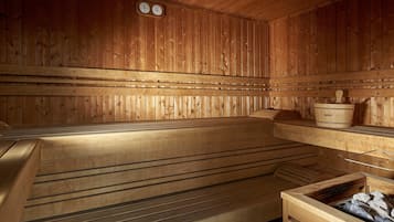 A wooden sauna with benches, a wooden bucket, and a stone-filled container.