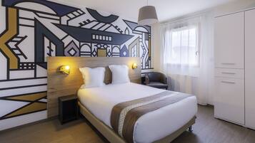 A modern hotel room with a large bed, a headboard with geometric wall art, bedside lamps, a chair, and a wardrobe.