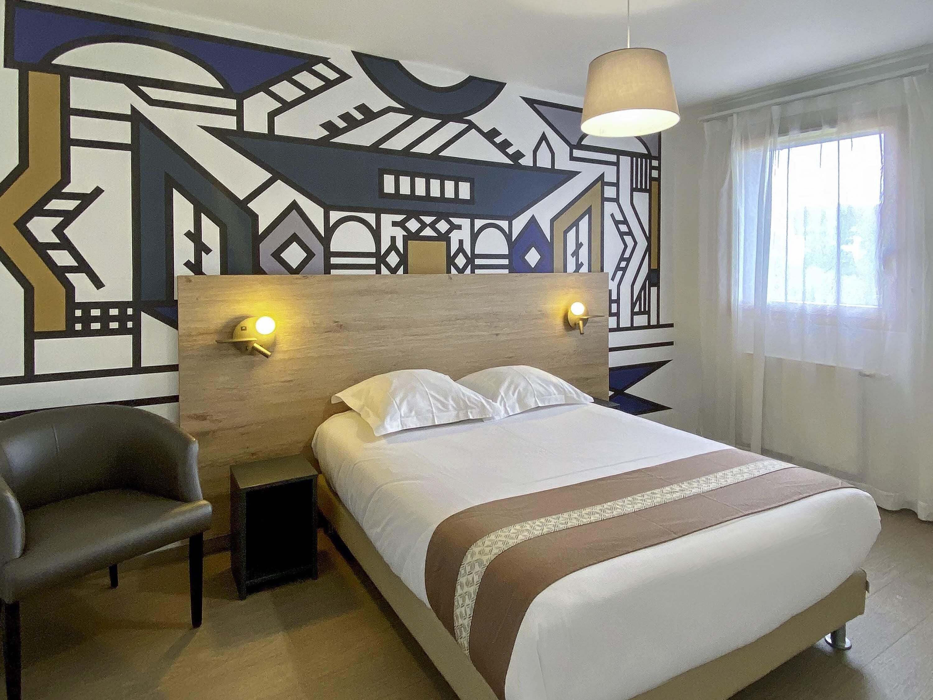 A hotel room with a bed, a chair, a nightstand, and a wall with a geometric pattern.