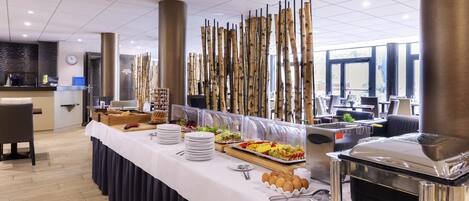 A buffet setup with various food items, a coffee machine, and a seating area with tables and chairs.