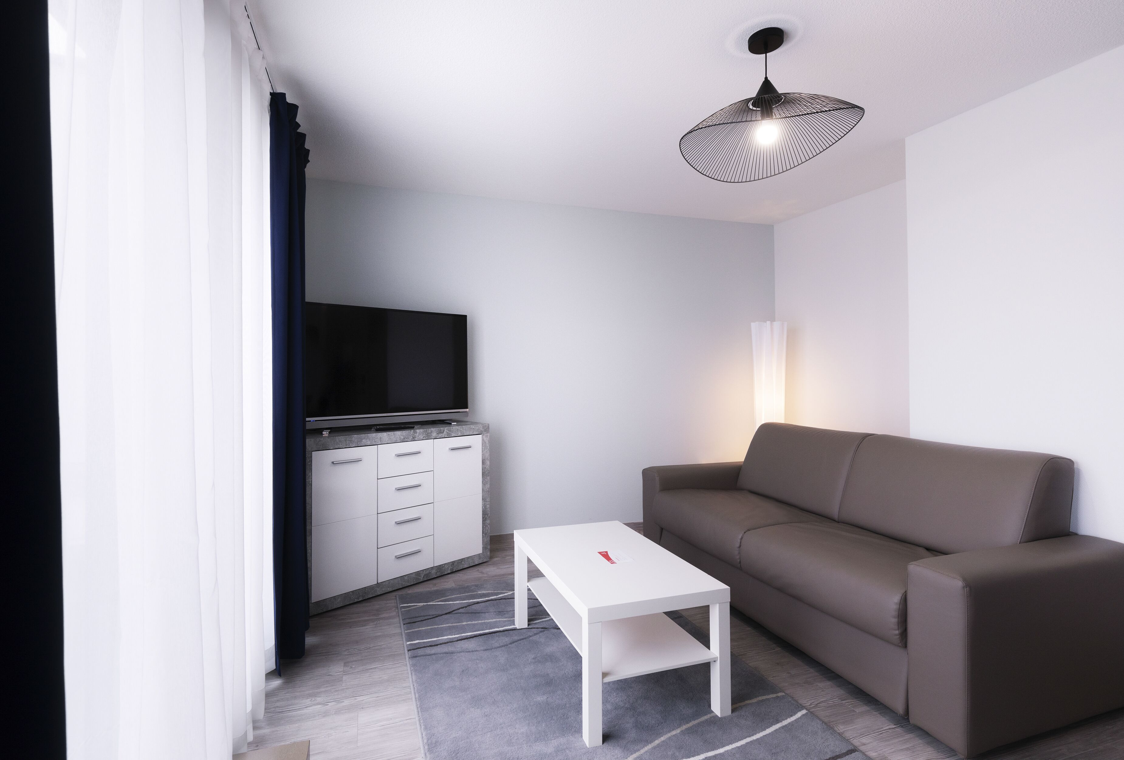 A modern living room with a sofa, a TV mounted on a cabinet, a white coffee table, and a patterned rug.
