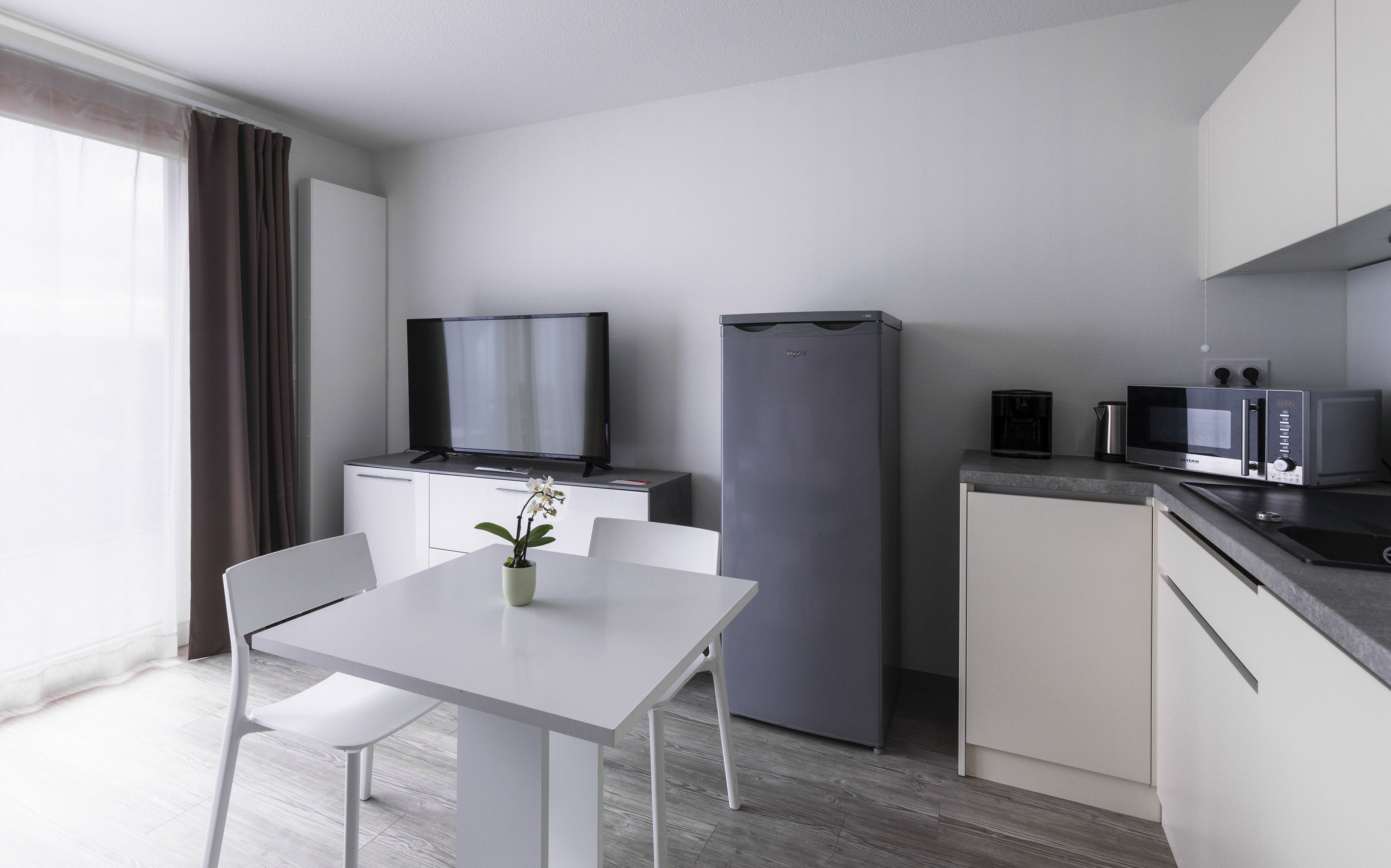 A modern kitchen with a dining table, chairs, a refrigerator, a microwave, and a television.
