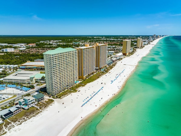 An aerial view of a coastal area with a beach, high-rise buildings, and a clear blue sky.