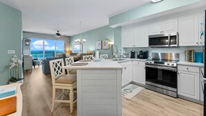 Una cocina moderna con armarios blancos, una isla central, electrodomésticos de acero inoxidable y vistas al exterior.