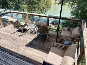 A wooden deck with outdoor furniture, including chairs and a table, overlooking a body of water. - River Haven: lakefront home with dock and kayaks (McQueeney)