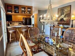 A dining area with a glass table, wicker chairs, a chandelier, and a painting on the wall. - River Haven: lakefront home with dock and kayaks (McQueeney)