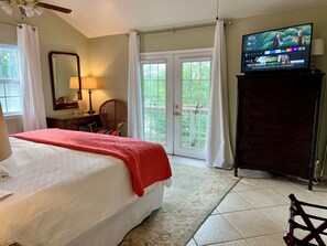A hotel room with a bed, a television, a desk, a chair, and a view of the outdoors through a sliding door. - River Haven: lakefront home with dock and kayaks (McQueeney)