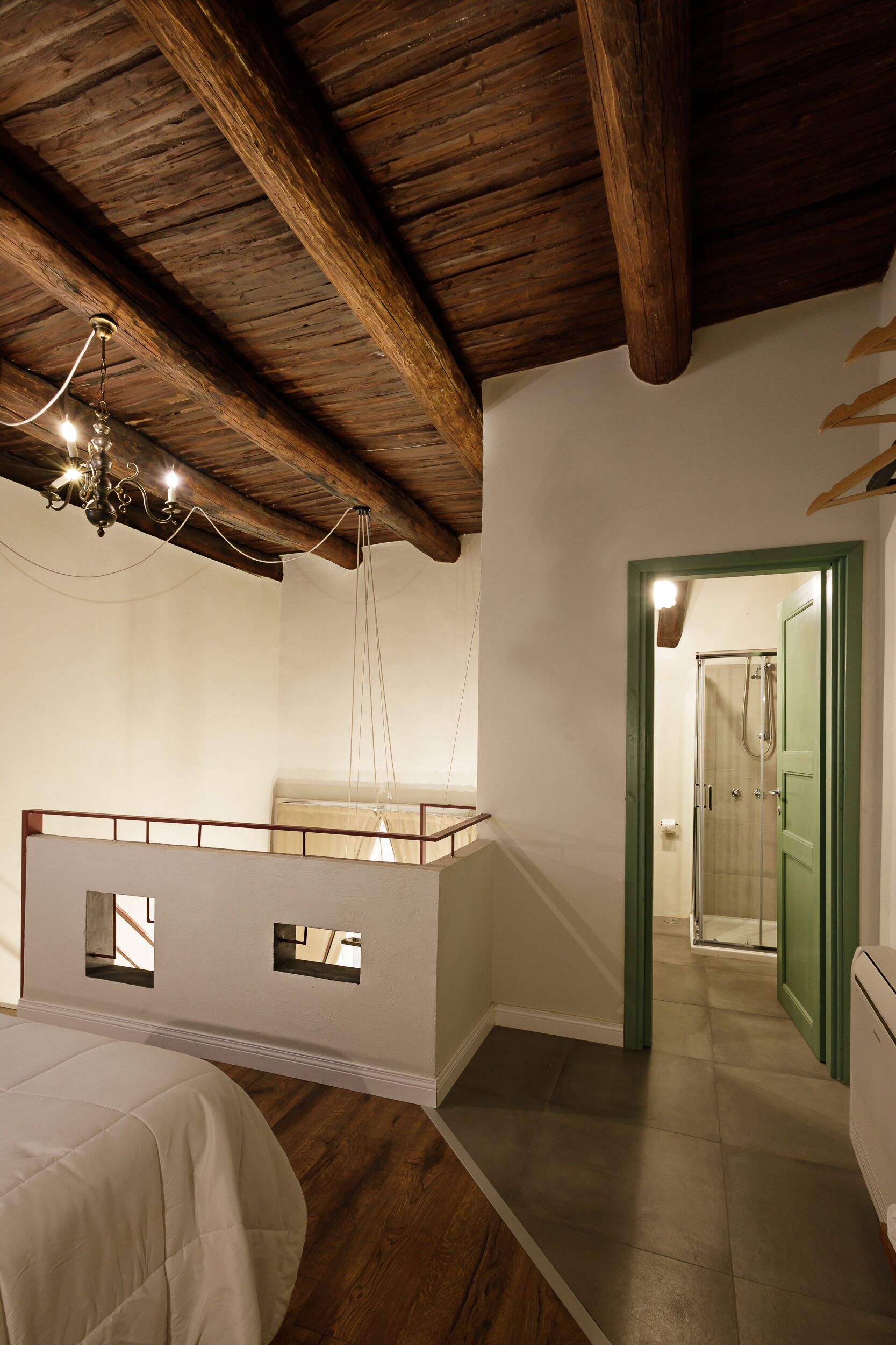 A bedroom with a bunk bed, wooden beams, a chandelier, and a bathroom door.