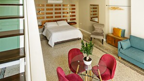 Um quarto espaçoso com cama, sofá, mesa de jantar com cadeiras e escada para um andar superior.
