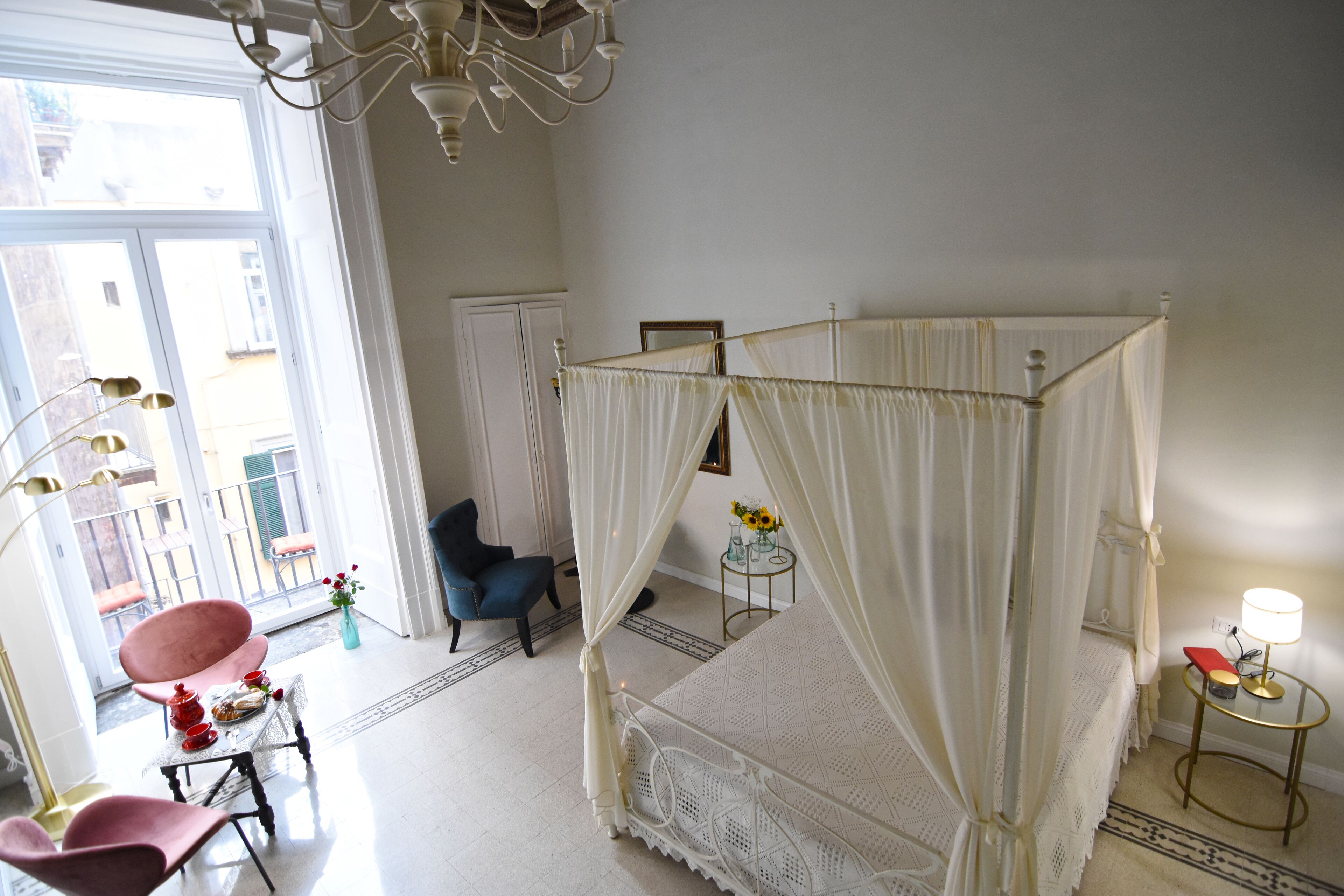 Ein Schlafzimmer mit einem Himmelbett, einem Sessel, einem kleinen Tisch mit Lampe und Blick auf den Balkon.