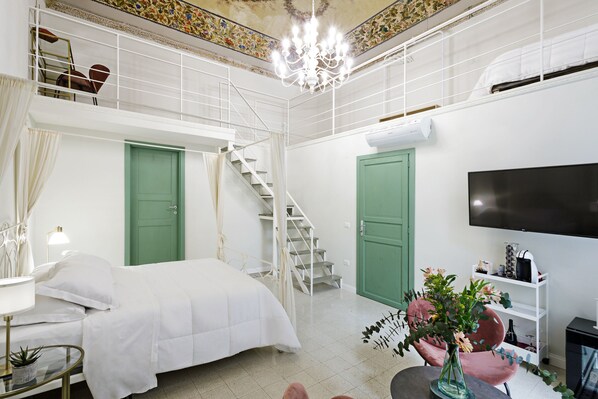 A bedroom with a bed, a TV, a staircase, and a green door. - Pala Suites (Naples)