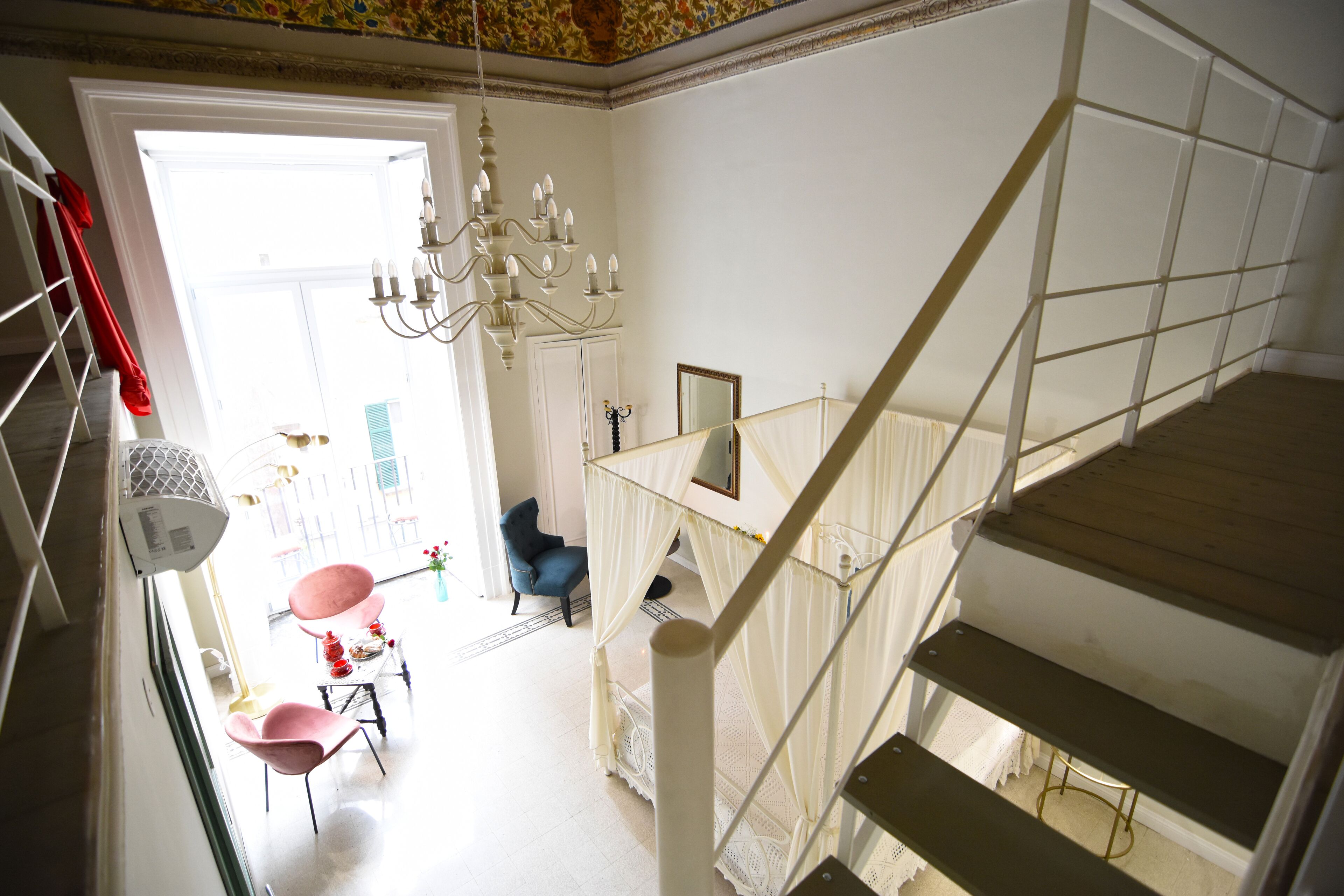 Un escalier avec une rampe blanche, un lustre et une chaise bleue dans une pièce dotée d’une porte blanche et d’une fenêtre.