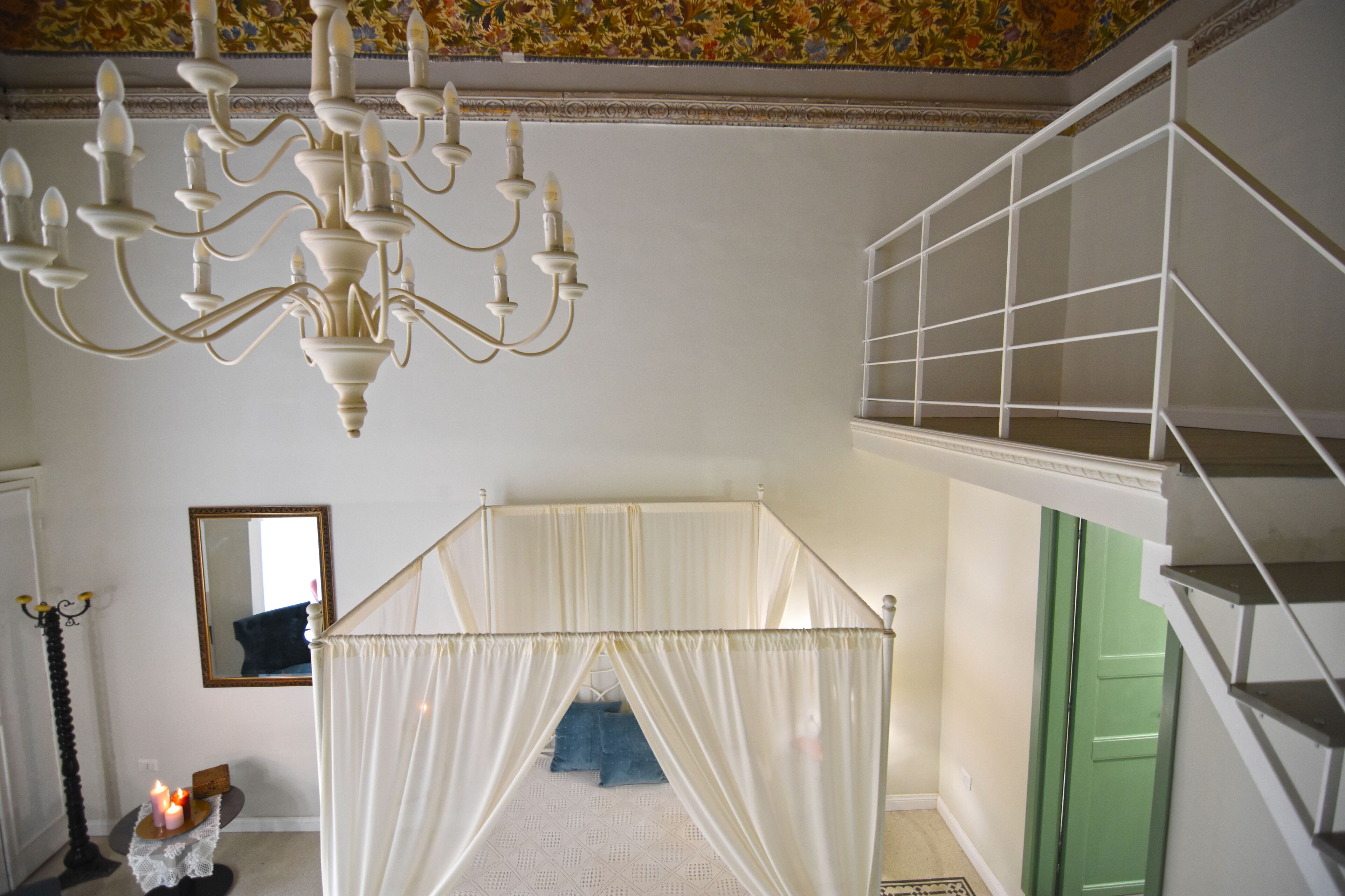 A room with a canopy bed, a chandelier, a green door, and a staircase.