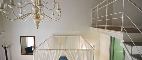 A room with a canopy bed, a chandelier, a green door, and a staircase.