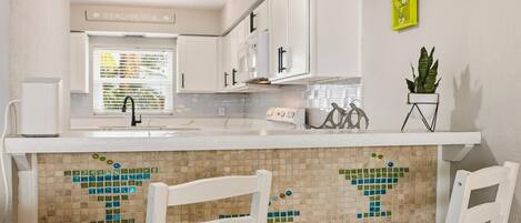 A kitchen with white cabinets, a tiled backsplash, and a window with blinds.