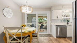 Een moderne keuken met witte kasten, een roestvrijstalen koelkast, en een eethoek met een gele tafel en stoelen.
