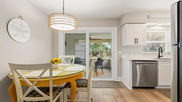 A modern kitchen with white cabinets, a stainless steel refrigerator, and a dining area with a yellow table and chairs.