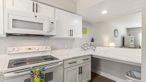 Een moderne keuken met witte kasten, een ingebouwde magnetron, een fornuis en een spoelbak.