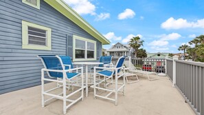 Une terrasse avec des chaises blanches et une table, une maison bleue et un ciel dégagé.