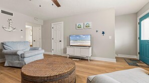 A living room with a grey sofa, a TV on a white cabinet, a wicker ottoman, and a blue door. - Beachy Townhome ~ Pet Friendly ~ Steps to the Beach!!! (Saint Augustine)