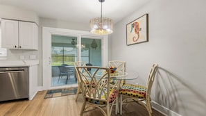 Una cocina moderna con armarios blancos, lavavajillas de acero inoxidable y una mesa de comedor de vidrio con sillas de colores.