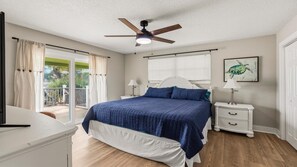 A bedroom with a bed, bedside tables, a ceiling fan, a window with blinds, and a balcony with curtains.
