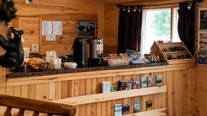 A wooden cabin interior with a wooden counter, a coffee machine, a bear decoration, and a window with curtains. - Sunshine Motel and Cabins (Ontonagon)