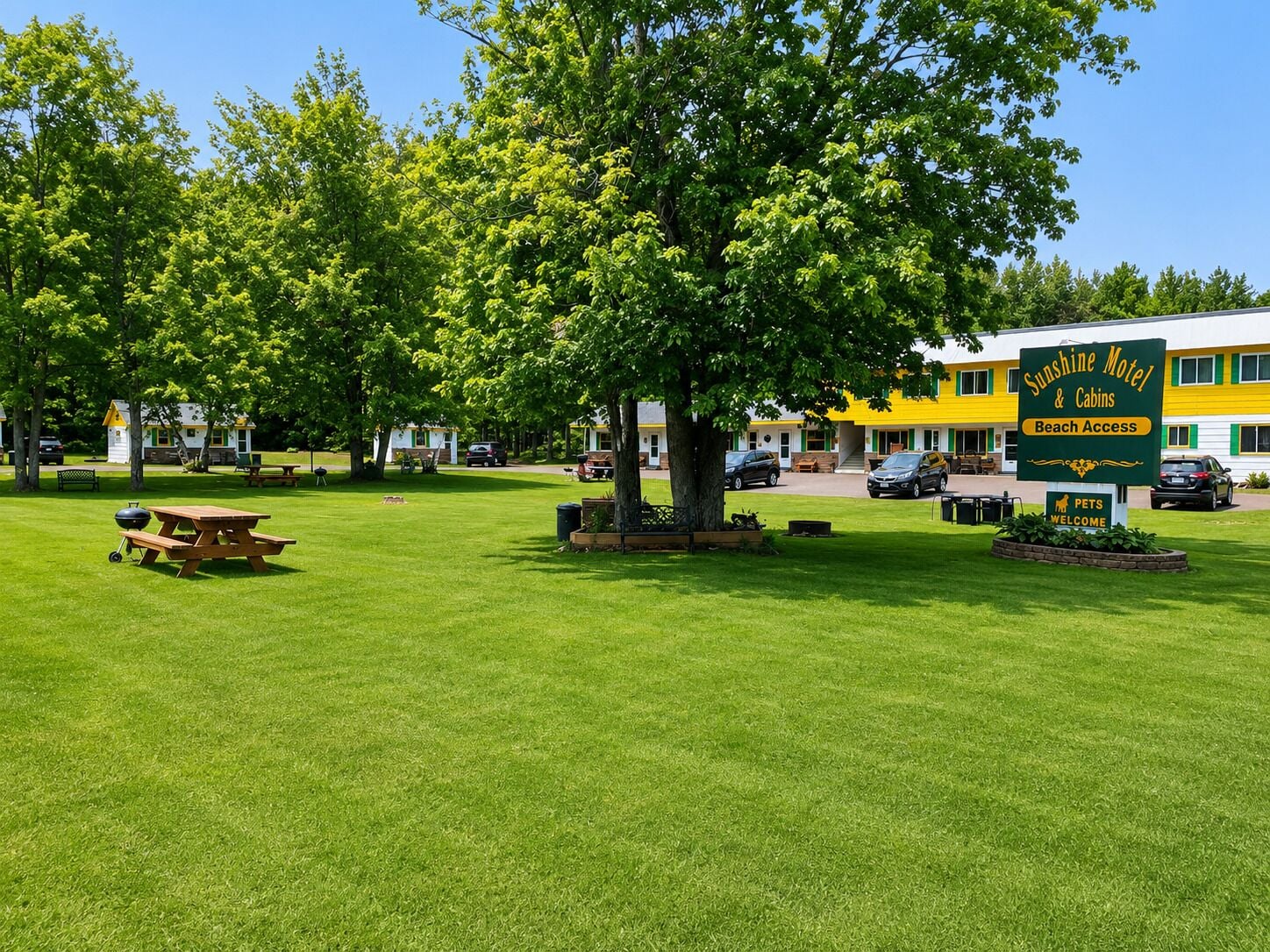 A motel with a green sign indicating beach access, a picnic table, and a well-maintained lawn.