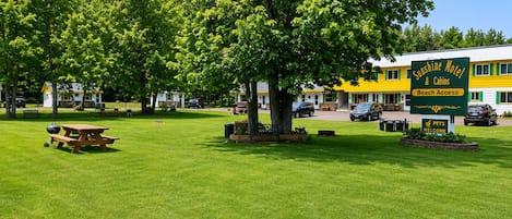 A motel with a green sign indicating beach access, a picnic table, and a well-maintained lawn.