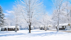 A snow-covered landscape with multiple cabins, each with a distinct architectural style, surrounded by bare trees. - Sunshine Motel and Cabins (Ontonagon)