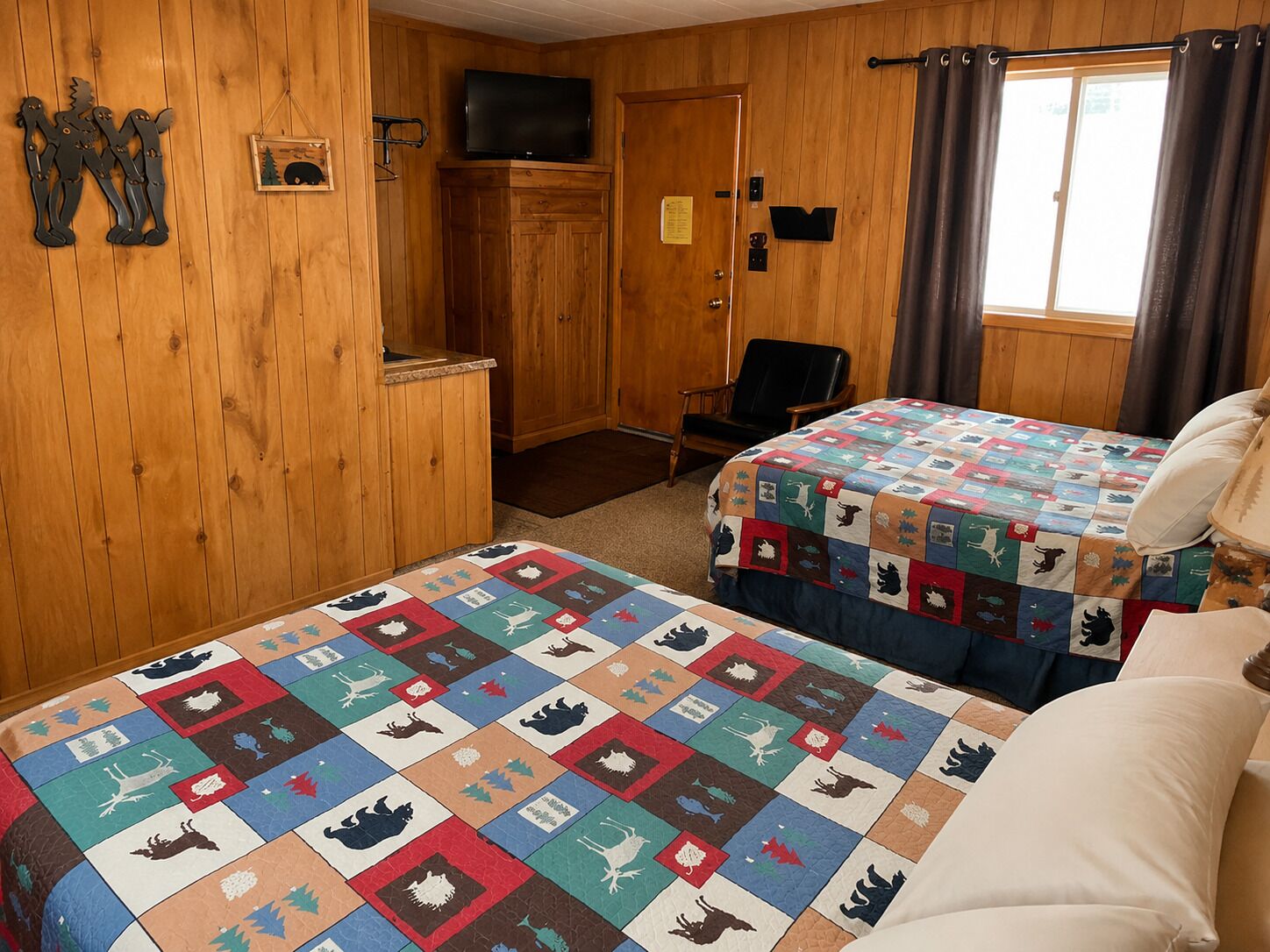 Een kamer met houten lambrisering, een bed met sprei, een stoel, een televisie en een raam met gordijnen.